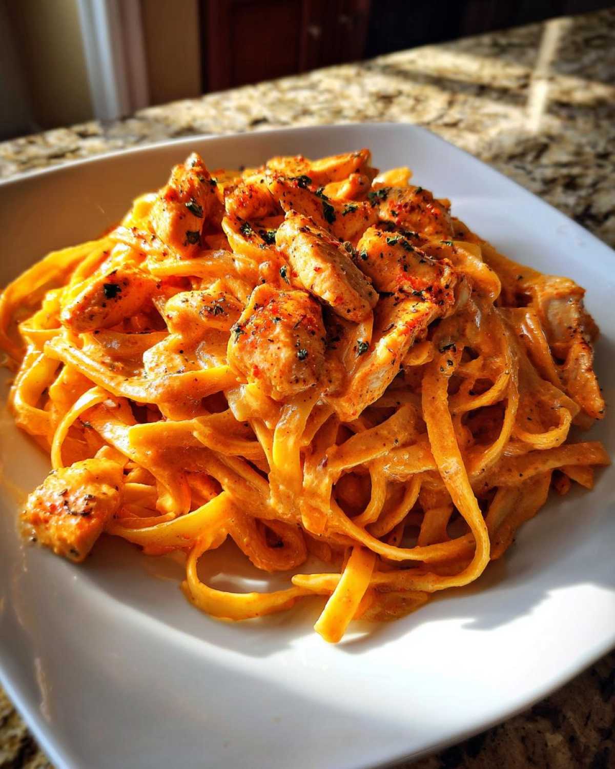 Close-up of a serving of Creamy Cajun Chicken Pasta with fettuccine noodles coated in a rich orange sauce and topped with seasoned chicken pieces.