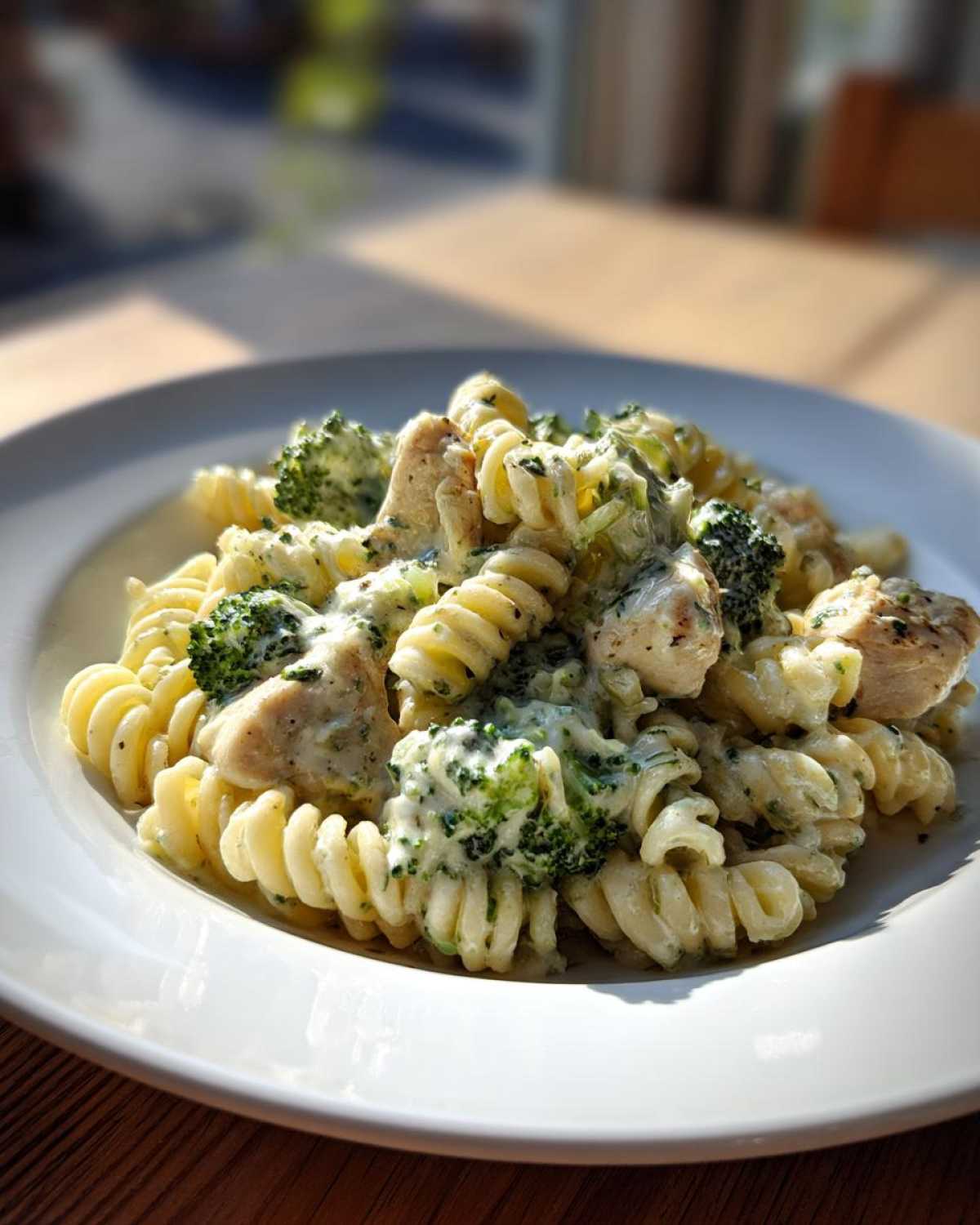 A close-up of a white bowl filled with Creamy Chicken and Broccoli Pasta Dinner featuring fusilli pasta, chunks of chicken, and bright green broccoli florets.
