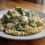 A close-up of a serving of Creamy Chicken and Broccoli Pasta Dinner featuring fusilli pasta, chunks of chicken, and bright green broccoli florets in a rich white sauce.