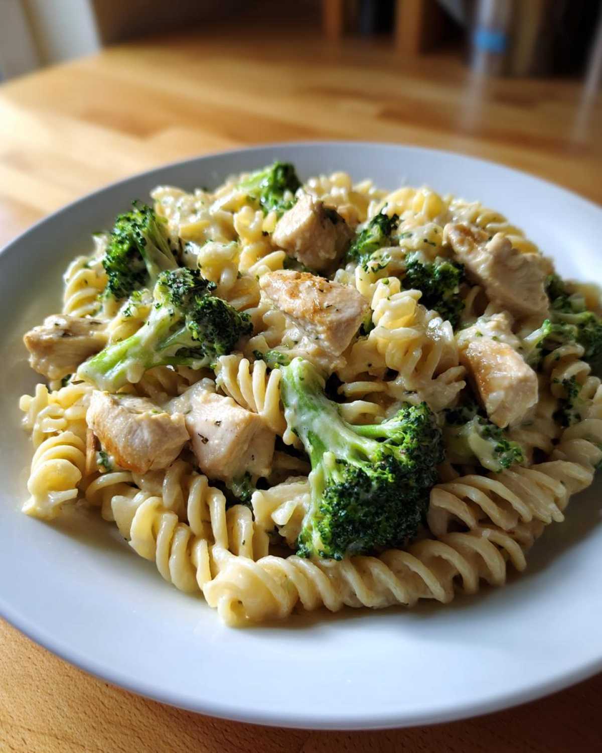 A close-up of a white plate filled with Creamy Chicken and Broccoli Pasta Dinner featuring rotini pasta, chunks of chicken, and bright green broccoli florets.