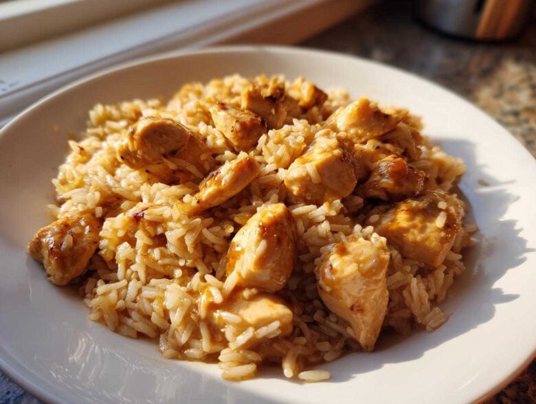 A close-up of a white plate filled with creamy chicken and rice skillet comfort meal, featuring tender chicken pieces coated in sauce.