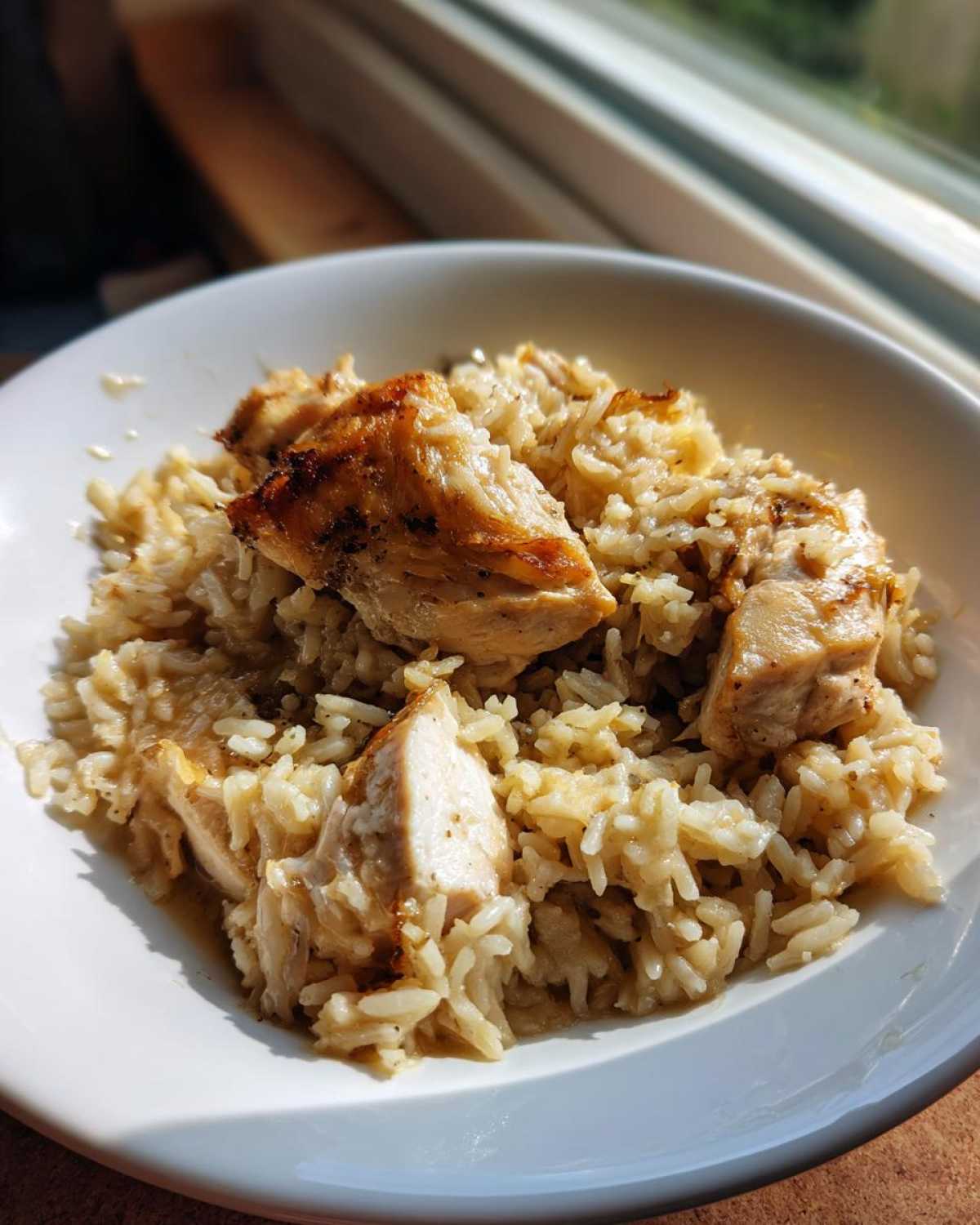 Close-up of a white bowl filled with creamy chicken and rice skillet comfort meal, topped with seared chicken pieces.