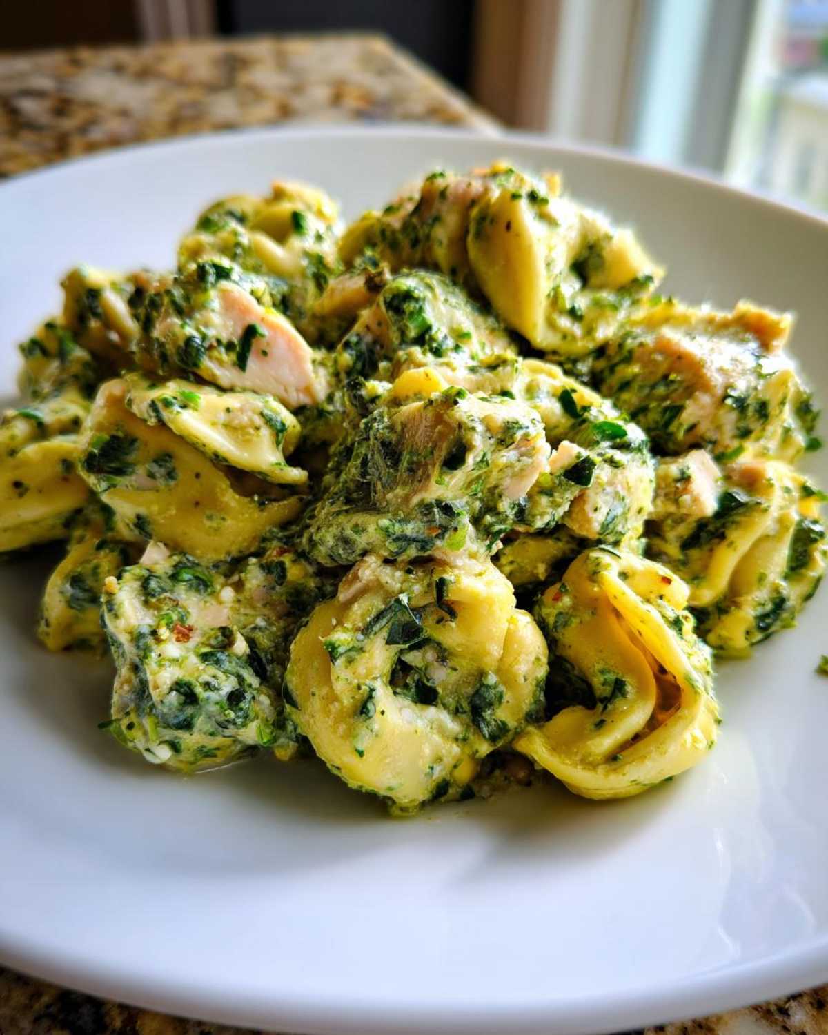 A close-up of tortellini pasta mixed with chunks of chicken and coated in a thick, green, creamy chicken tortellini with spinach sauce.