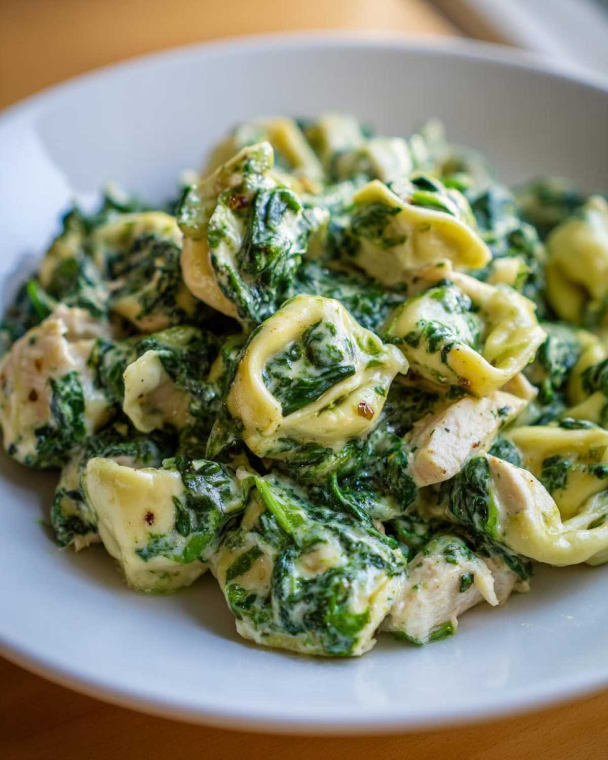 Close-up of tortellini pasta coated in a rich, creamy spinach sauce with pieces of chicken, ready to eat.