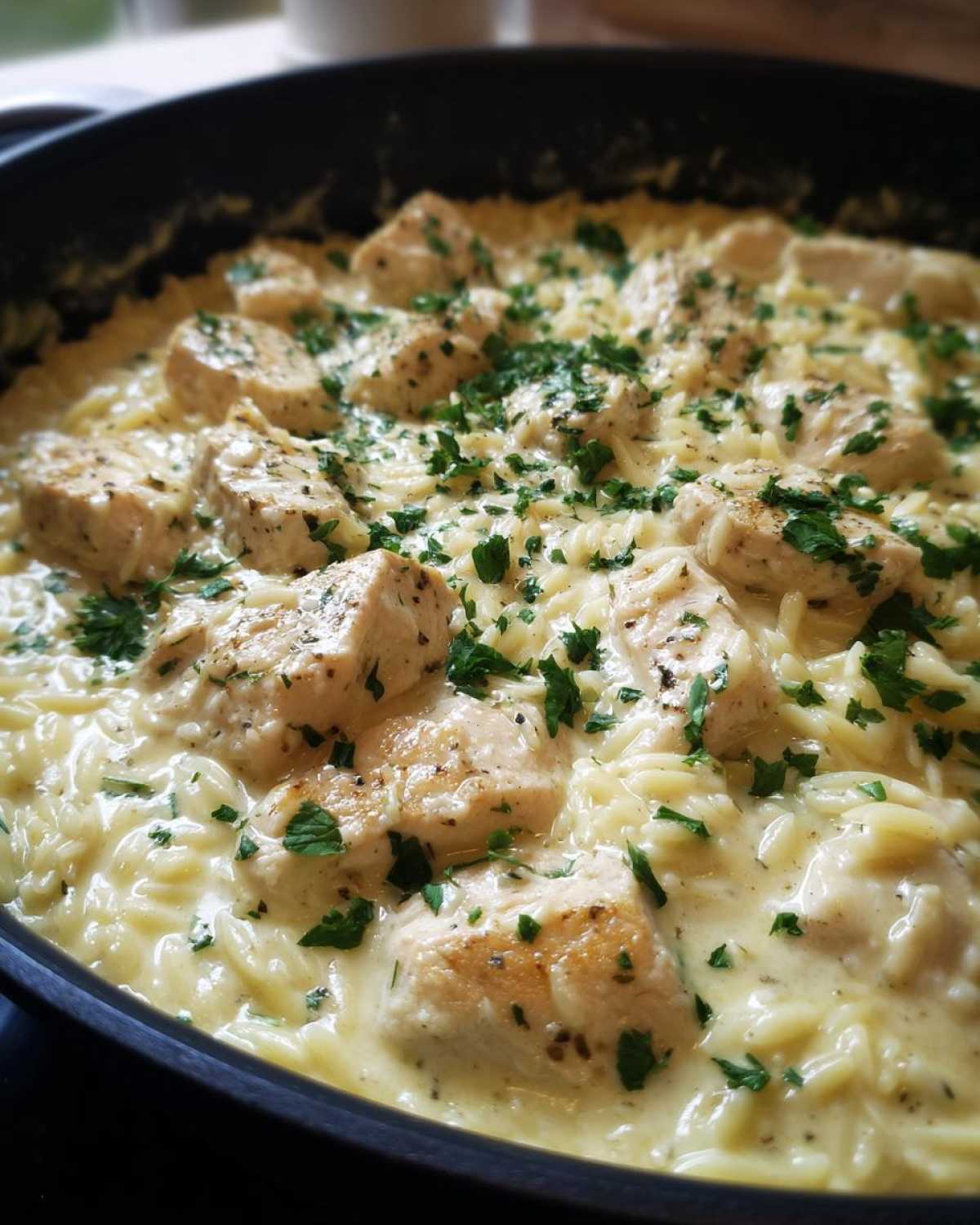 Close-up of Creamy Garlic Parmesan Orzo with Chicken topped with fresh parsley in a black skillet.