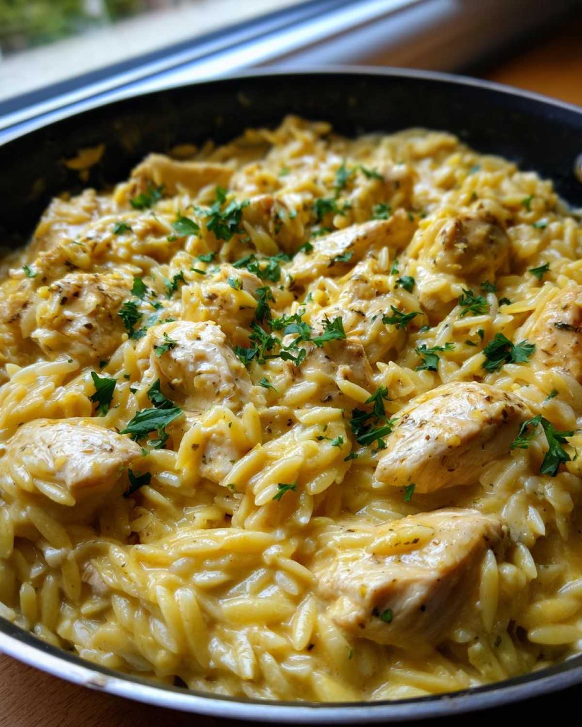 Close-up of creamy garlic parmesan orzo with chicken pieces, garnished with fresh parsley, served in a black skillet.