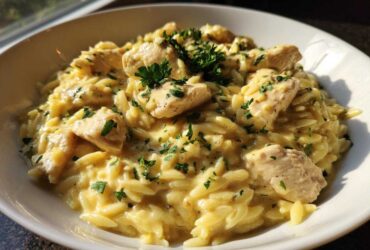 A close-up of Creamy Garlic Parmesan Orzo with Chicken, topped with fresh parsley, served in a white bowl.
