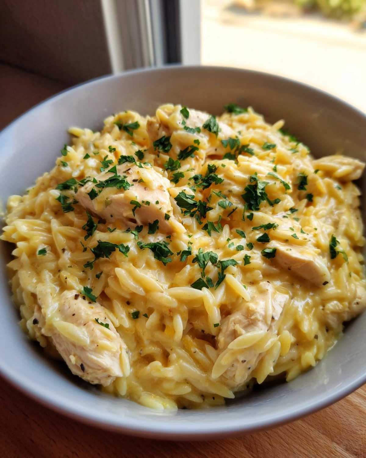 A close-up of a bowl filled with creamy garlic parmesan orzo with chicken pieces, topped with fresh parsley.