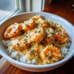 A close-up of a white bowl filled with white rice topped generously with Creamy Garlic Shrimp.