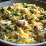 Close-up of a bowl of Creamy Lemon Chicken Orzo pasta topped generously with chopped fresh herbs.