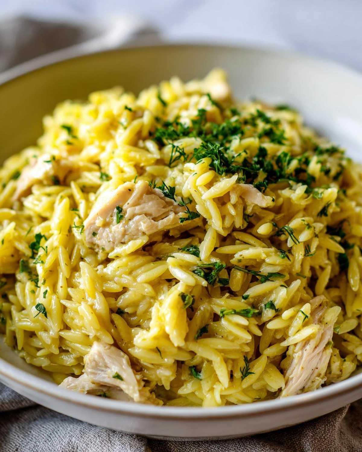 Close-up of a bowl filled with Creamy Lemon Chicken Orzo, topped generously with fresh chopped parsley.