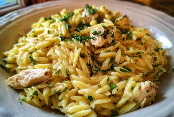 A close-up of a bowl of Creamy Lemon Chicken Orzo, featuring rice-shaped pasta, chunks of chicken, and fresh green herbs.