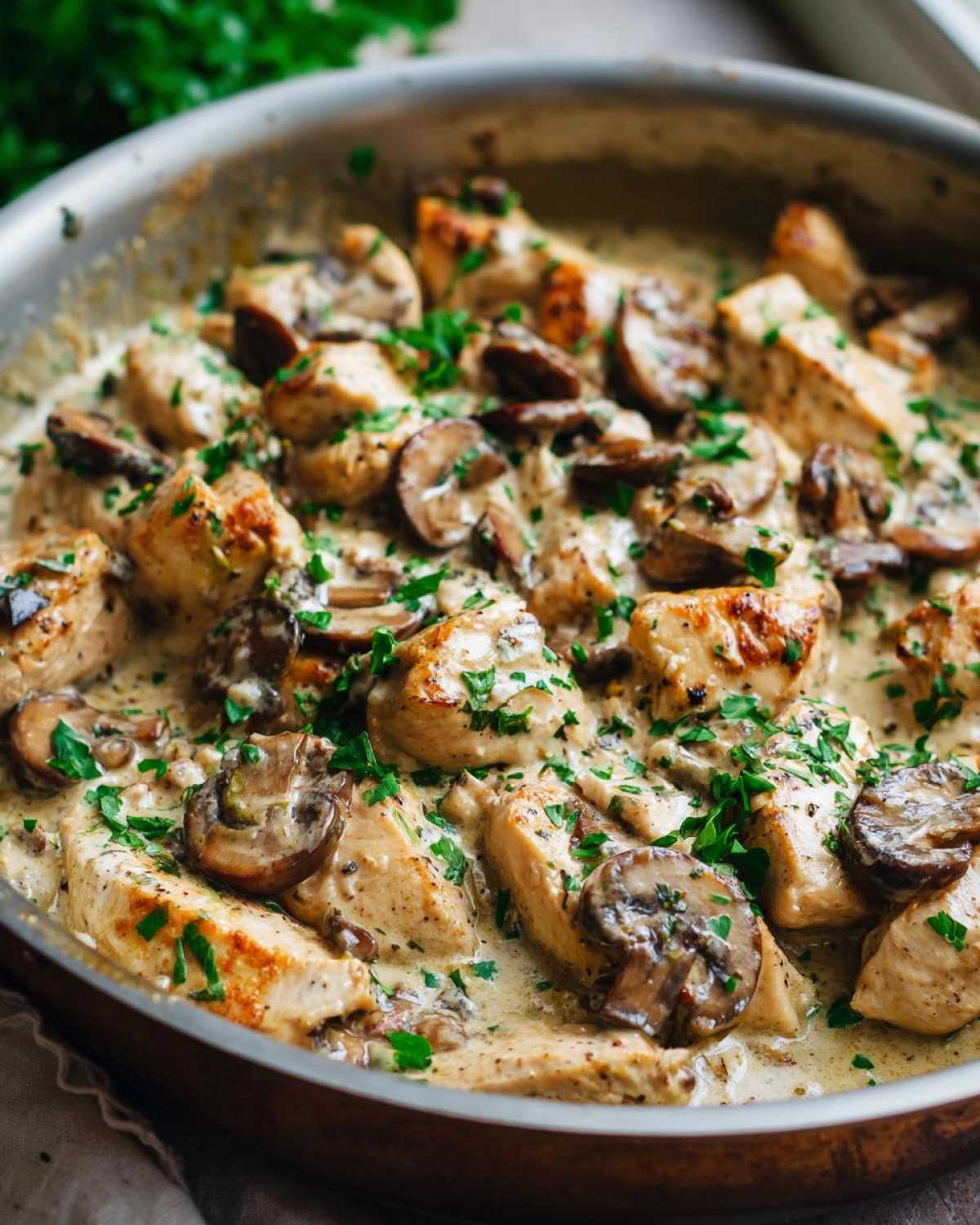 Close-up of pan-seared chicken pieces and sliced mushrooms coated in a rich, creamy sauce, garnished with parsley for a Creamy Mushroom Chicken Skillet.