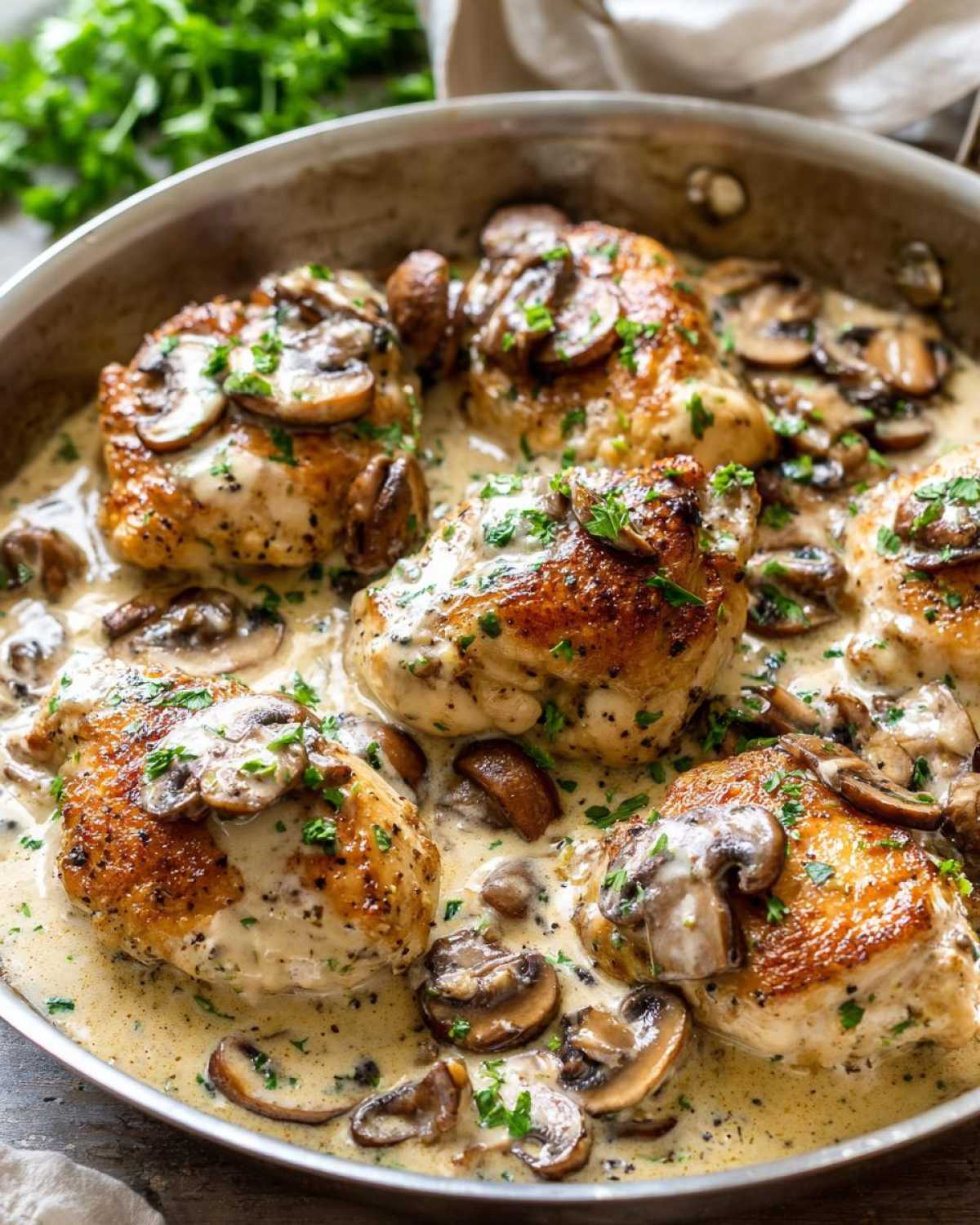 Five pieces of golden-brown chicken thighs swimming in a rich, creamy mushroom sauce in a skillet.