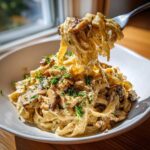 A fork lifts a generous portion of Creamy Mushroom Pasta with Parmesan Sauce, topped with sautéed mushrooms and fresh parsley.