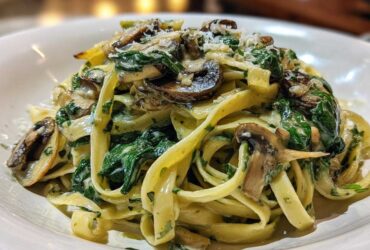 A close-up of fettuccine pasta tossed in a creamy sauce with sautéed mushrooms and wilted spinach, topped with Parmesan cheese for a Creamy Spinach and Mushroom Pasta Dinner.