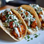 Close-up of three Crispy Chicken Tacos with Garlic Lime Sauce drizzled over fried chicken and cabbage.
