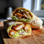A Crispy Chicken Wrap with Creamy Avocado Sauce cut in half, showing crispy chicken, lettuce, and avocado sauce.