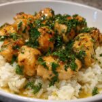 Close-up of tender chicken pieces coated in garlic butter sauce and fresh parsley served over white rice in a bowl.