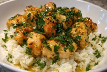 Close-up of tender chicken pieces coated in garlic butter sauce and fresh parsley served over white rice in a bowl.