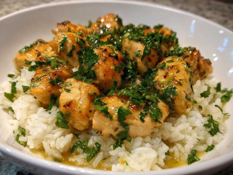Close-up of tender chicken pieces coated in garlic butter sauce and fresh parsley served over white rice in a bowl.