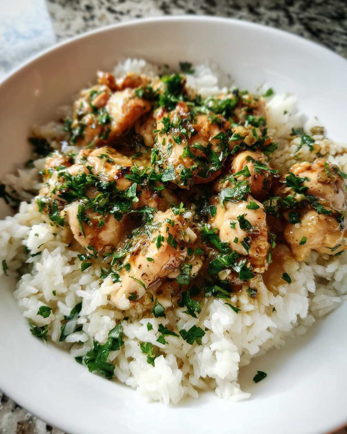 A close-up of Garlic Butter Chicken and Rice One Pot Dinner served in a white bowl, topped with fresh parsley.