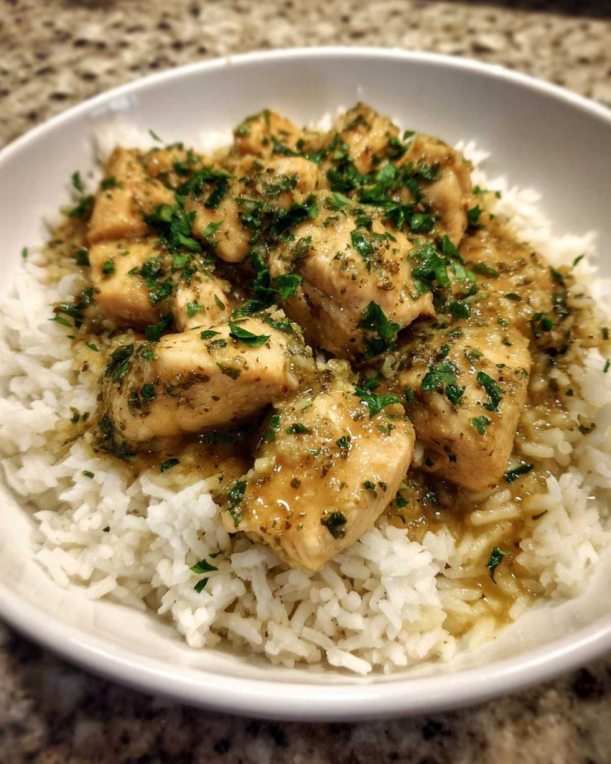 A close-up of Garlic Butter Chicken and Rice One Pot Dinner served in a white bowl, topped with fresh parsley.