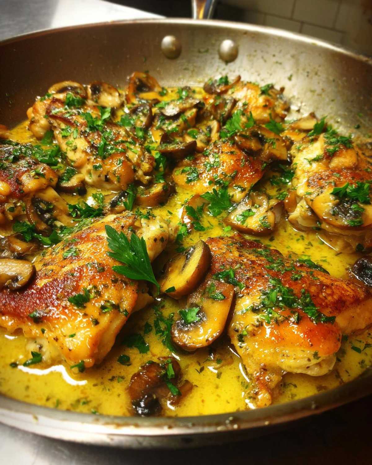Close-up of golden-brown chicken pieces simmering in a rich garlic butter sauce with sliced mushrooms, garnished with parsley for a Garlic Butter Chicken and Mushroom Skillet Dinner.