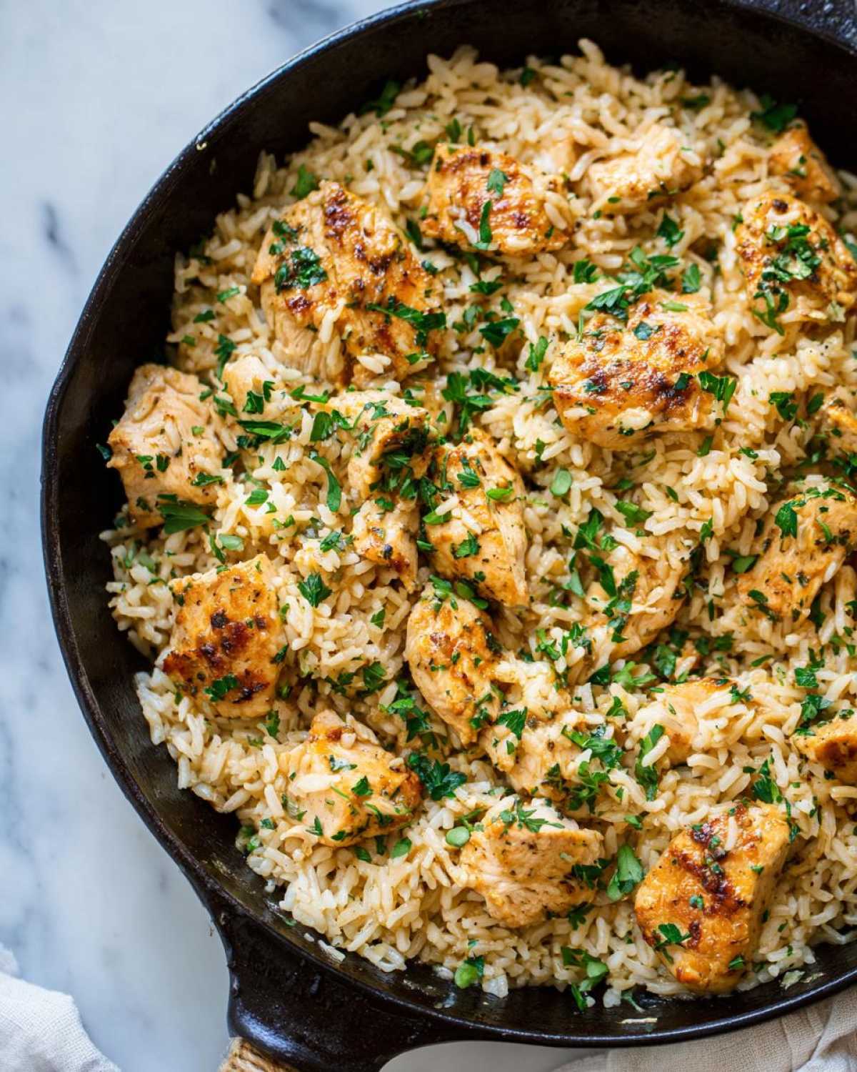 Overhead view of Garlic Butter Rice with Chicken Skillet, featuring browned chicken pieces mixed with seasoned rice and topped with fresh parsley.