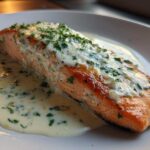 A perfectly cooked fillet of Garlic Butter Salmon resting in a pool of creamy lemon sauce, topped with fresh parsley.