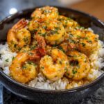 Close-up of juicy Garlic Butter Shrimp and Rice topped with fresh parsley in a dark bowl.
