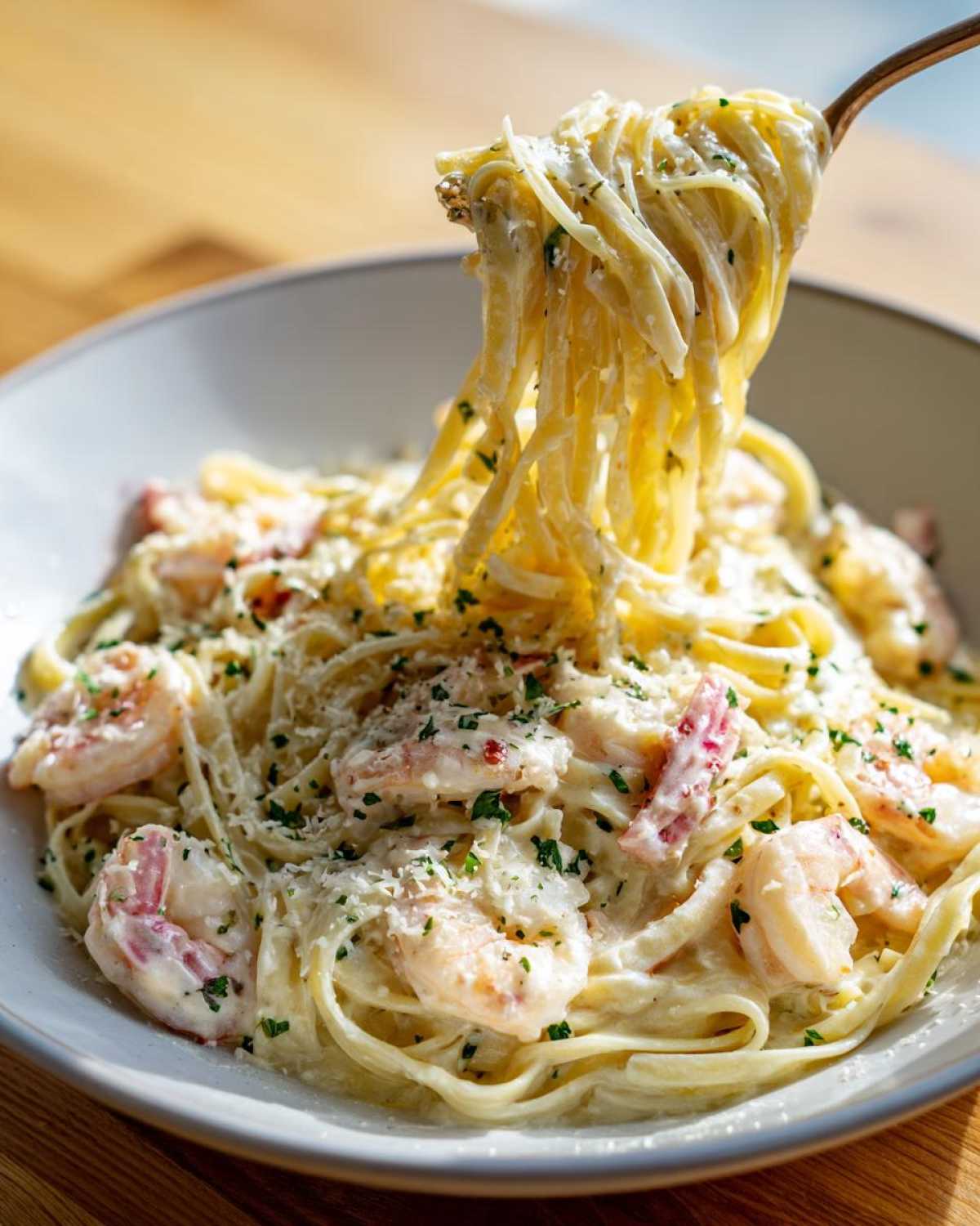 A fork twirling linguine noodles coated in rich cream sauce from a bowl of Garlic Butter Shrimp Pasta with Cream Sauce.