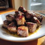 A mound of perfectly seared Garlic Butter Steak Bites glistening in sauce on a white plate.