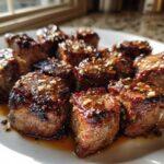 Close-up of perfectly seared Garlic Butter Steak Bites glistening with sauce and minced garlic on a white plate.