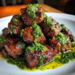 A close-up of seared Garlic Butter Steak Bites piled high and drizzled generously with bright green herb sauce.
