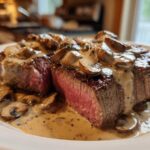 Two perfectly cooked steaks covered in creamy mushroom sauce, showcasing the medium-rare center of the Garlic Butter Steak with Creamy Mushroom Sauce.
