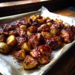 Close-up of glistening Honey BBQ Chicken Bake with roasted potatoes on a parchment-lined baking sheet.