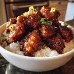 Close-up of glossy Honey Garlic Chicken Bites piled high over fluffy white rice, garnished with green onions.