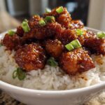 Close-up of glossy Honey Garlic Chicken Bites piled high on a bed of fluffy white rice and topped with sliced green onions.