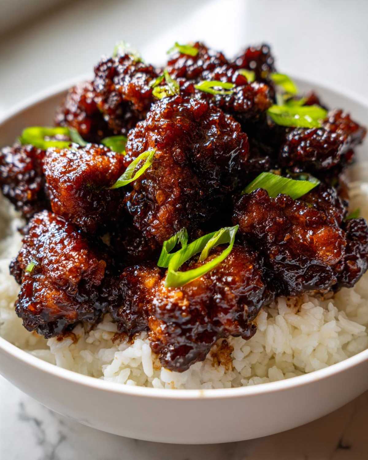 Close-up of sticky, glazed Honey Garlic Chicken Bites served over a bed of fluffy white rice, garnished with green onions.
