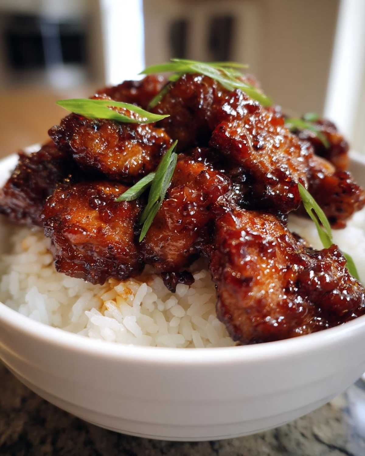 Close-up of sticky, glazed Honey Garlic Chicken Bites piled high on a bed of fluffy white rice and garnished with green onions.