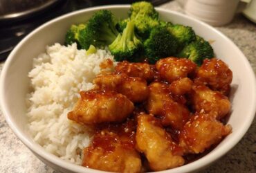 A close-up of a white bowl filled with Honey Garlic Chicken Bowl with Rice, topped with steamed broccoli florets.