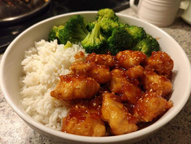 A close-up of a white bowl filled with Honey Garlic Chicken Bowl with Rice, topped with steamed broccoli florets.