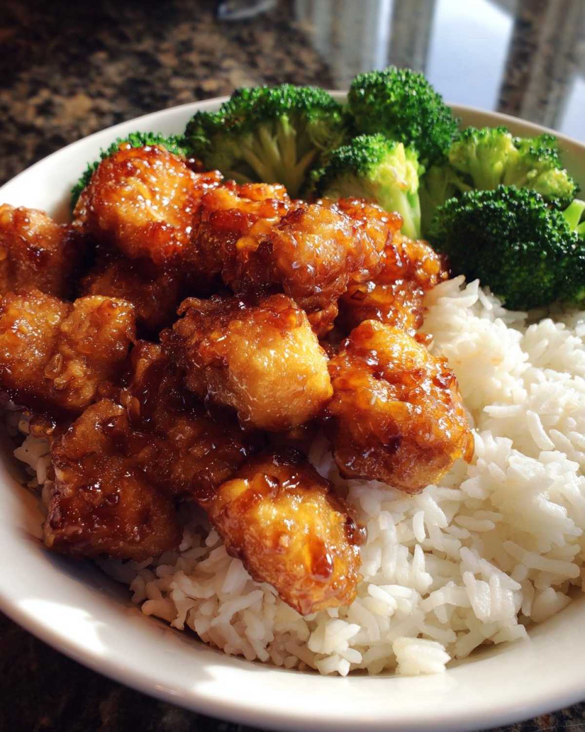 A close-up of a Honey Garlic Chicken Bowl with sticky glazed chicken pieces served over white rice and steamed broccoli florets.