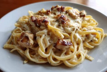 A close-up shot of fettuccine pasta coated in a rich cream sauce, topped with seared chicken pieces from the Honey Garlic Chicken Pasta.