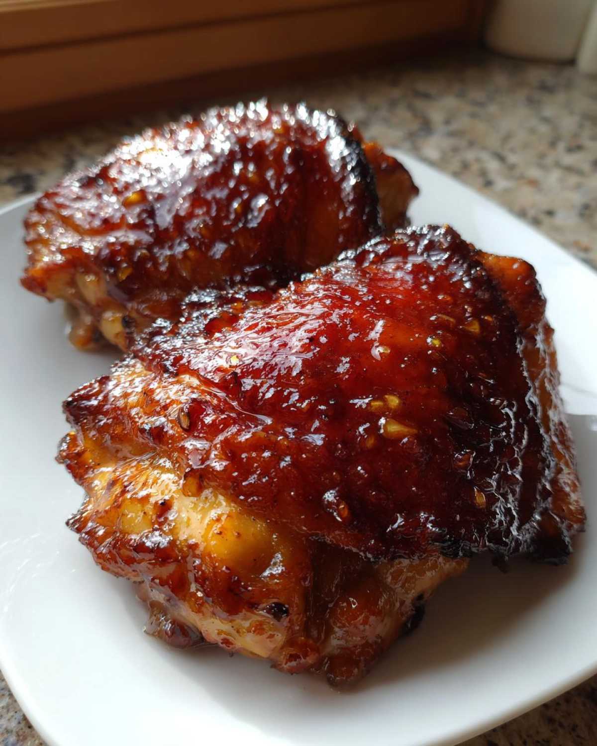 Two pieces of Honey Garlic Chicken Thighs Oven Baked, glistening with a dark, sticky glaze, served on a white plate.