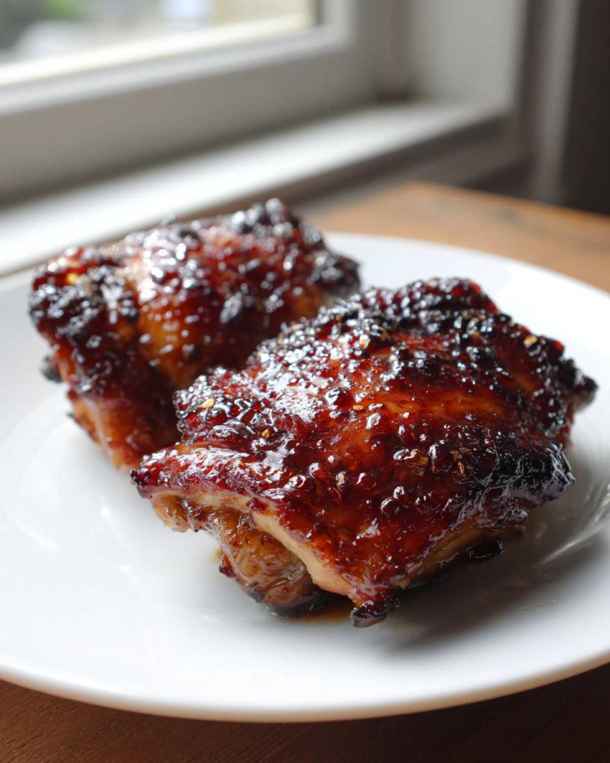 Two pieces of glistening Honey Garlic Chicken Thighs Oven Baked with a sticky, dark glaze on a white plate.