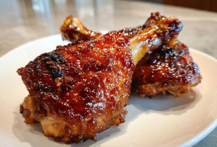 Close-up of two glistening, glazed Honey Garlic Chicken Thighs Oven Baked pieces on a white plate.