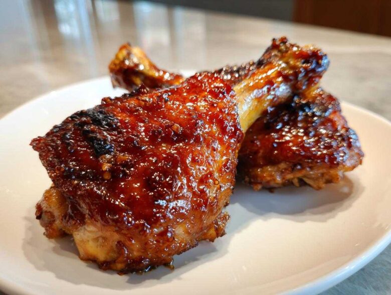 Close-up of two glistening, glazed Honey Garlic Chicken Thighs Oven Baked pieces on a white plate.
