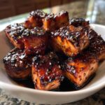 Close-up of shiny, caramelized Honey Garlic Salmon Bites stacked in a white bowl, sprinkled with sesame seeds.